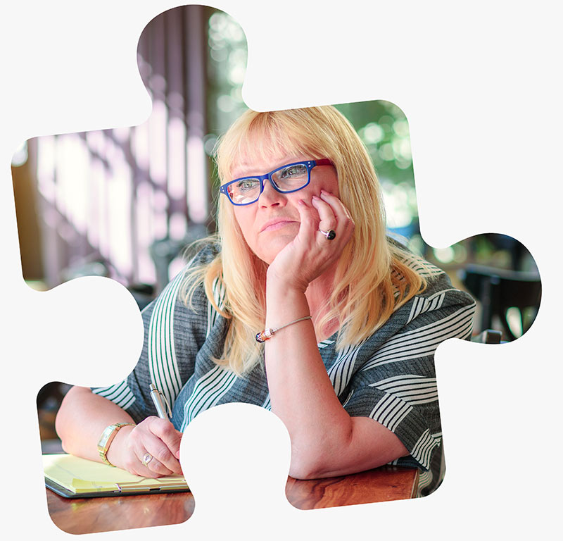 A woman sits thoughtfully at a coffee shop writing